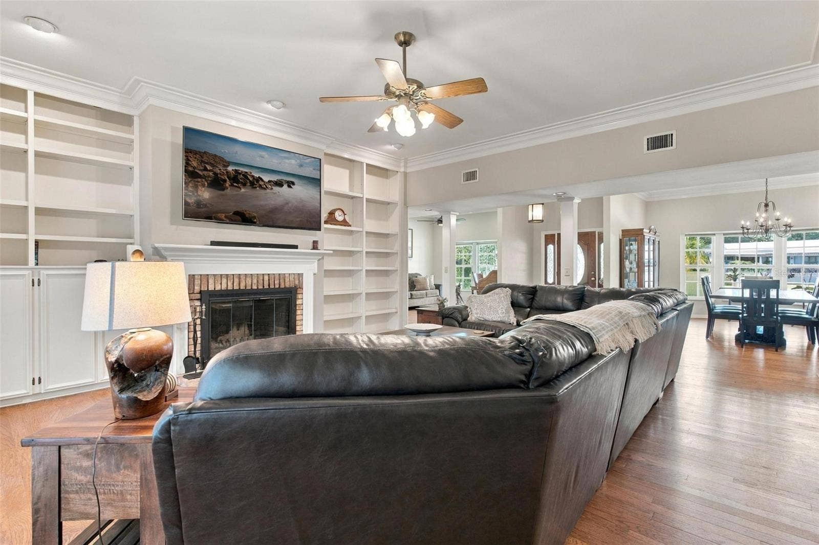 8732 SPRING COURT, Leesburg, FL 34788 Family Room features wood flooring, wood burning fireplace, built in shelving, and French door leading to screened enclosed lanai
