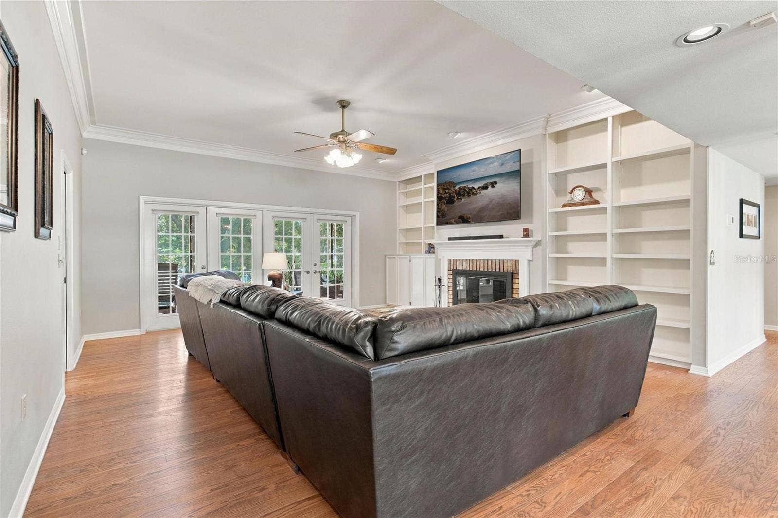 8732 SPRING COURT, Leesburg, FL 34788 Family Room features wood flooring, wood burning fireplace, built in shelving, and French door leading to screened enclosed lanai
