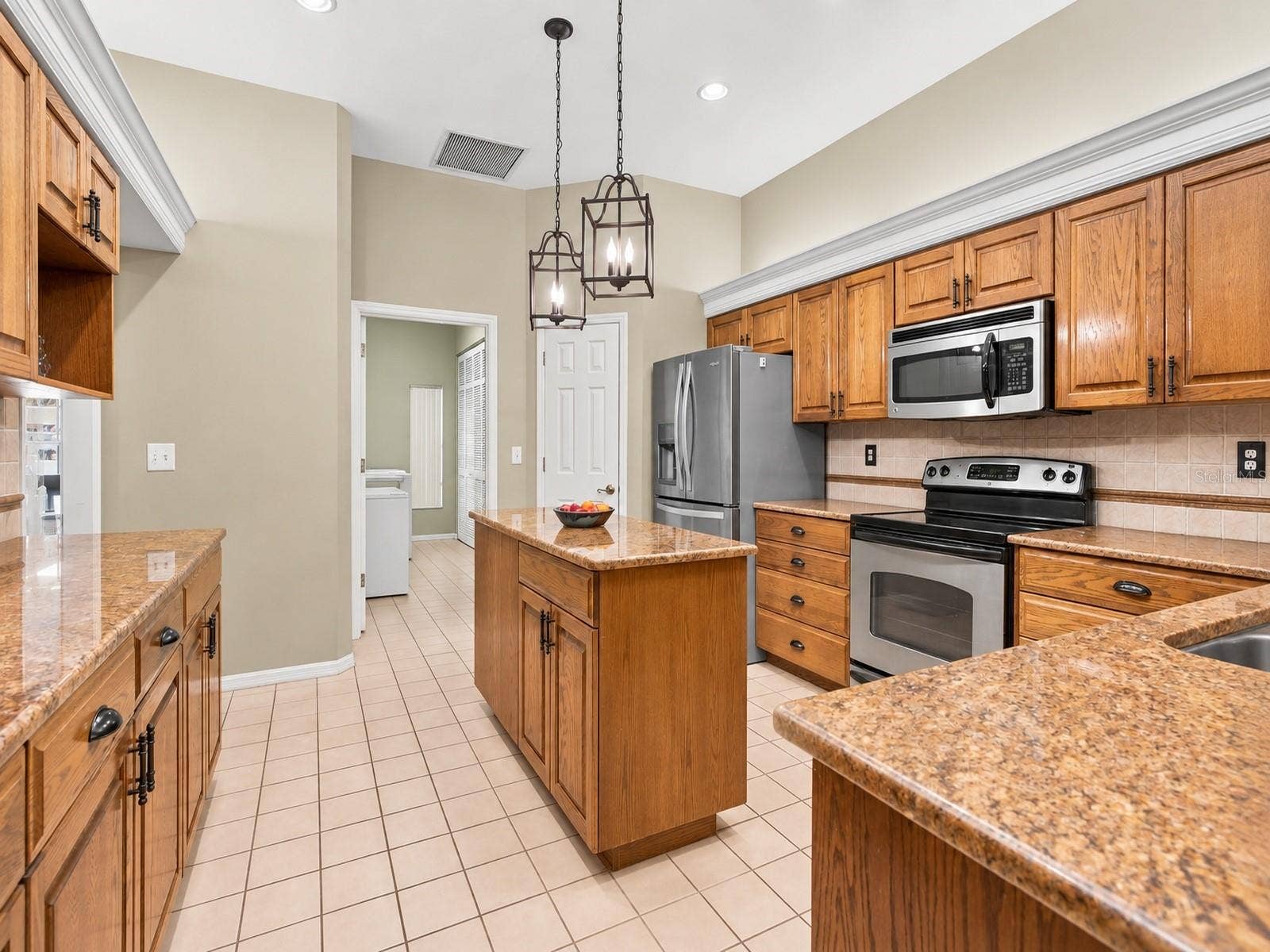 8732 SPRING COURT, Leesburg, FL 34788 Kitchen features oak cabinetry, center island, granite countertops, and stainless steel appliances.