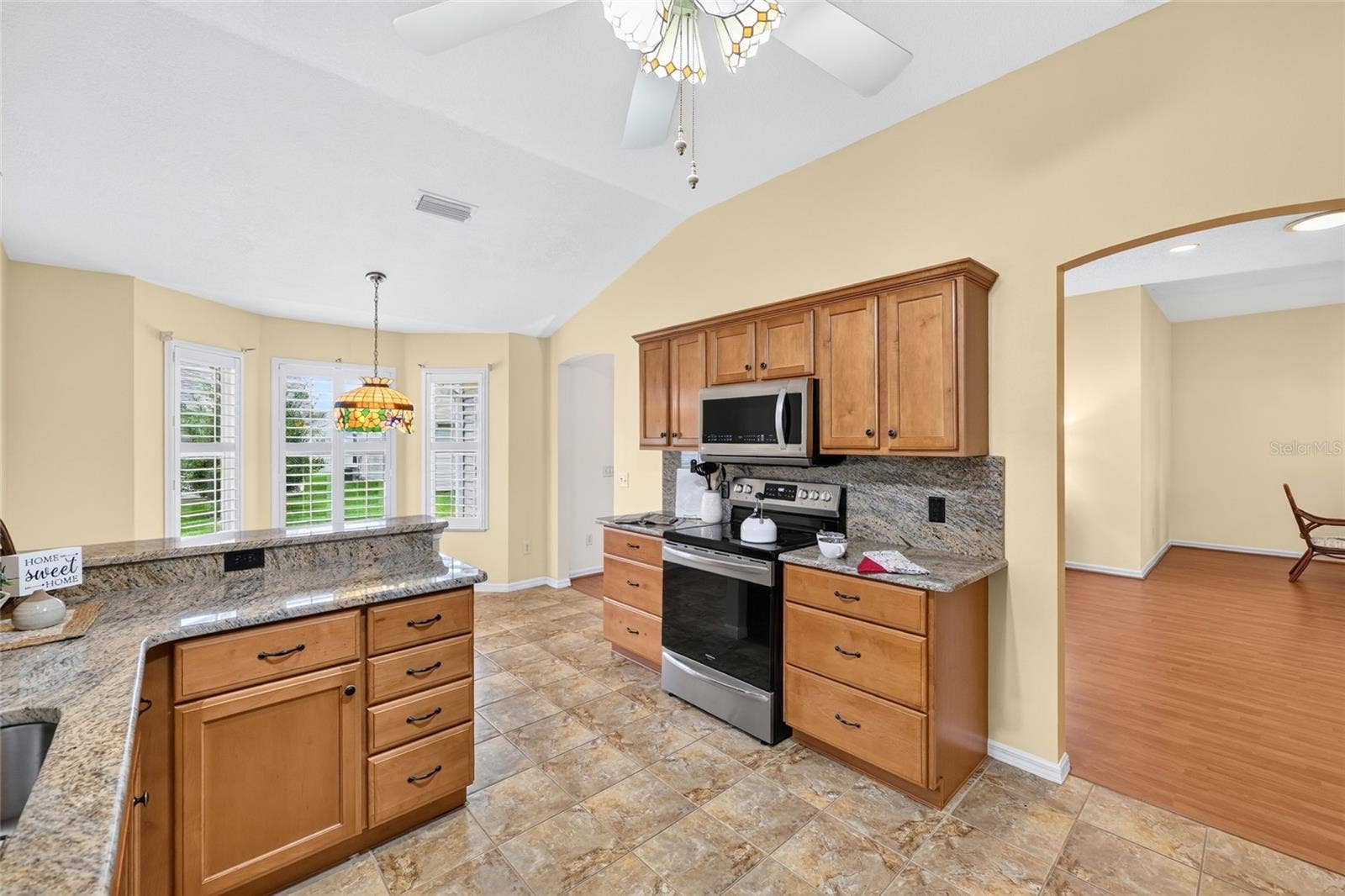 3064 BURBANK LANE, The Villages, FL 32162 Spacious kitchen featuring vaulted ceilings, generous cabinetry, granite countertops, tile flooring, and an adjoining breakfast nook filled with natural light.