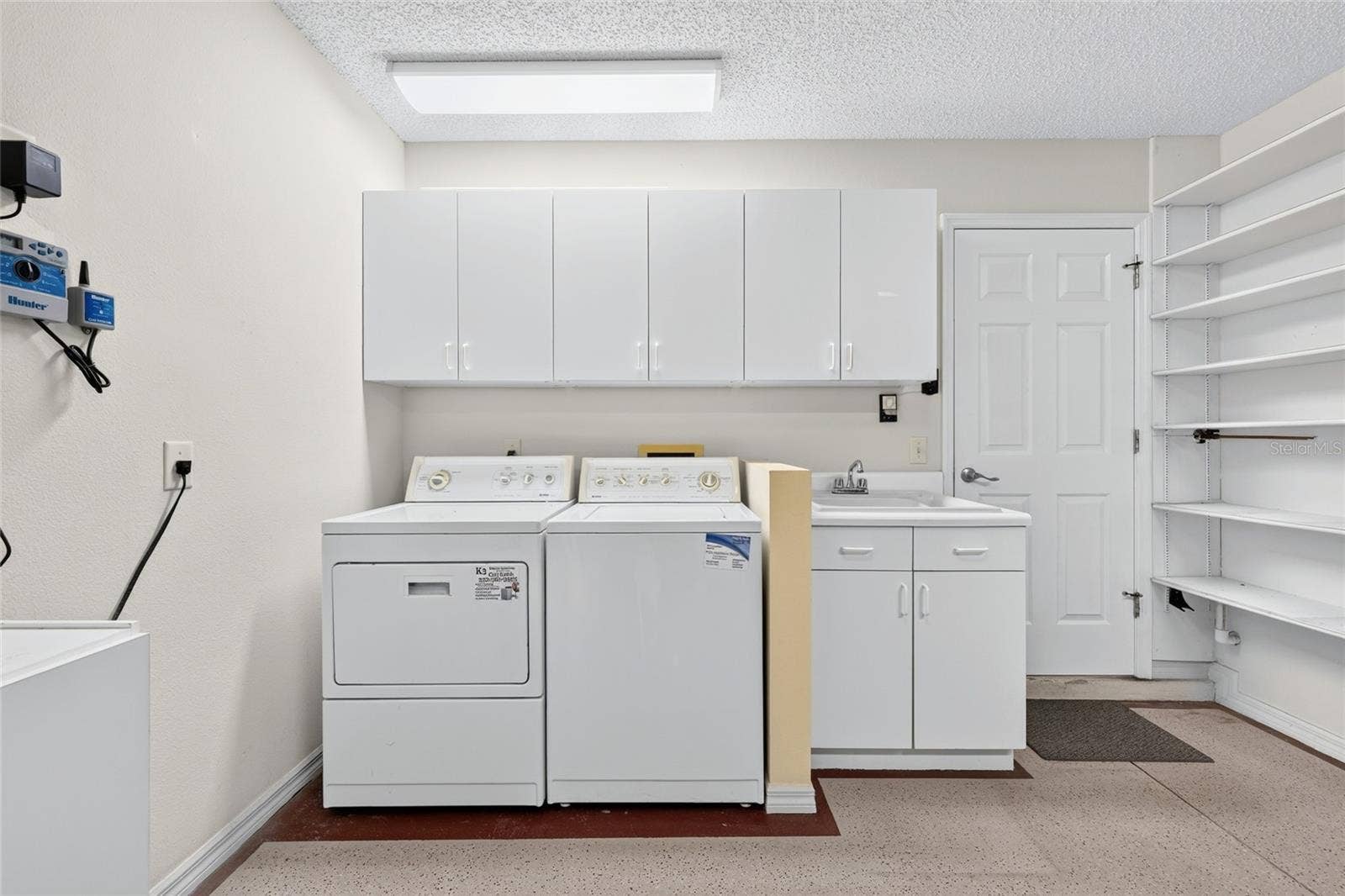 3064 BURBANK LANE, The Villages, FL 32162 Convenient laundry area featuring a washer and dryer, utility sink, overhead cabinetry, and open shelving for additional storage and organization.