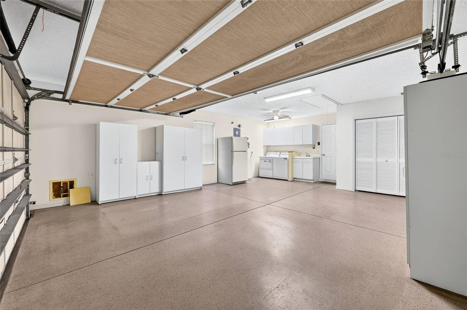 3064 BURBANK LANE, The Villages, FL 32162 Spacious two-car garage offering extensive storage cabinetry, a utility sink, laundry area, refrigerator, and room for vehicles and additional storage.