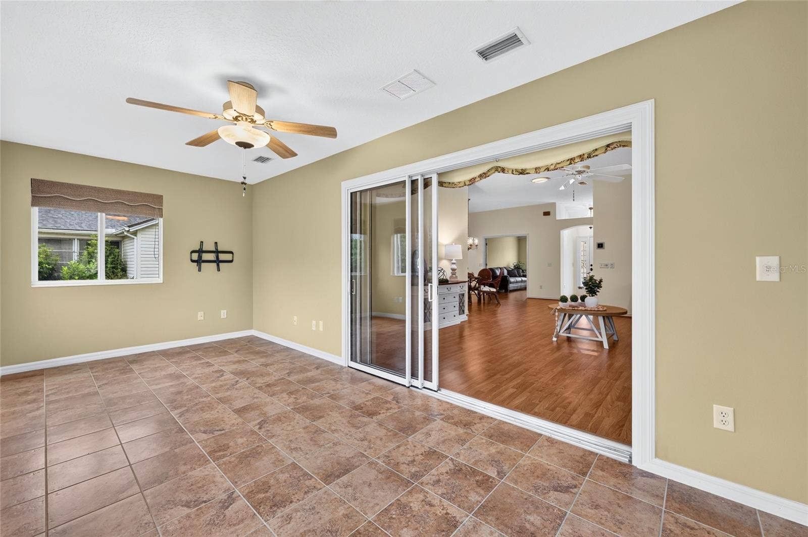 3064 BURBANK LANE, The Villages, FL 32162 Light-filled enclosed lanai featuring tile flooring, a ceiling fan, and sliding glass doors connecting to the main living area. A versatile space for relaxing or entertaining.