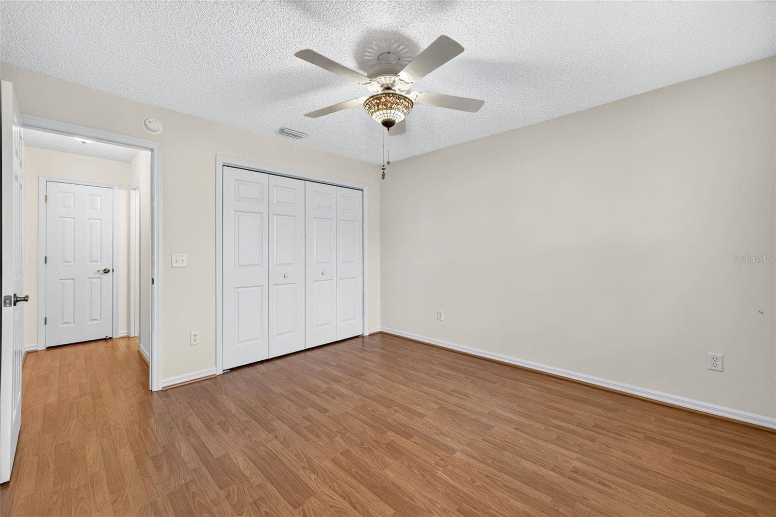 3064 BURBANK LANE, The Villages, FL 32162 Comfortable guest bedroom featuring wood-look flooring, a decorative ceiling fan, neutral walls, and a spacious double-door closet.
