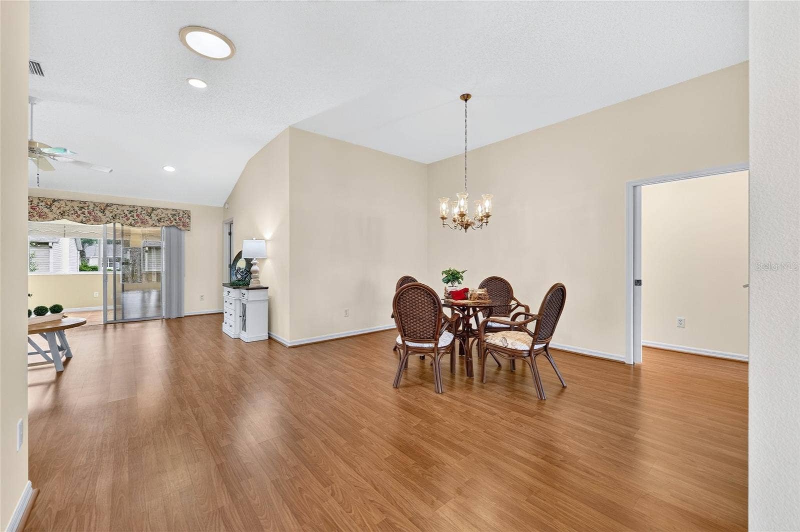 3064 BURBANK LANE, The Villages, FL 32162 Spacious dining area featuring wood-look flooring, vaulted ceilings, a decorative chandelier, and an open layout that flows into the living space.