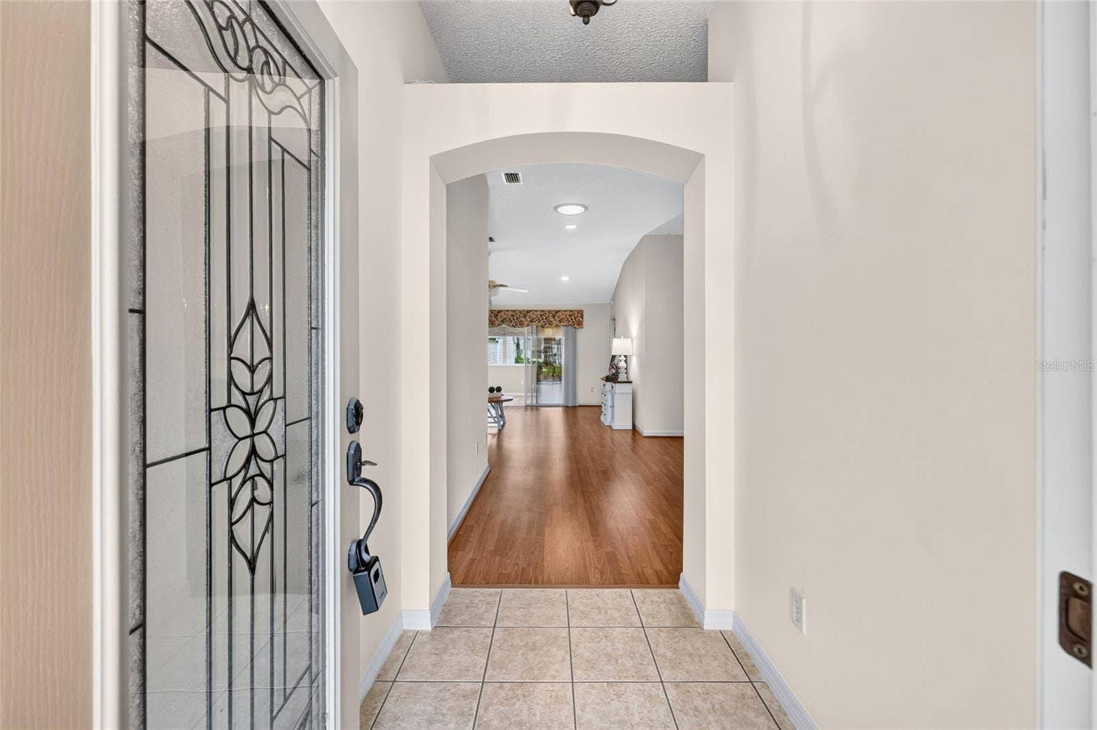 3064 BURBANK LANE, The Villages, FL 32162 Inviting foyer featuring a decorative glass front door, tile flooring, and an elegant arched opening leading into the main living area.