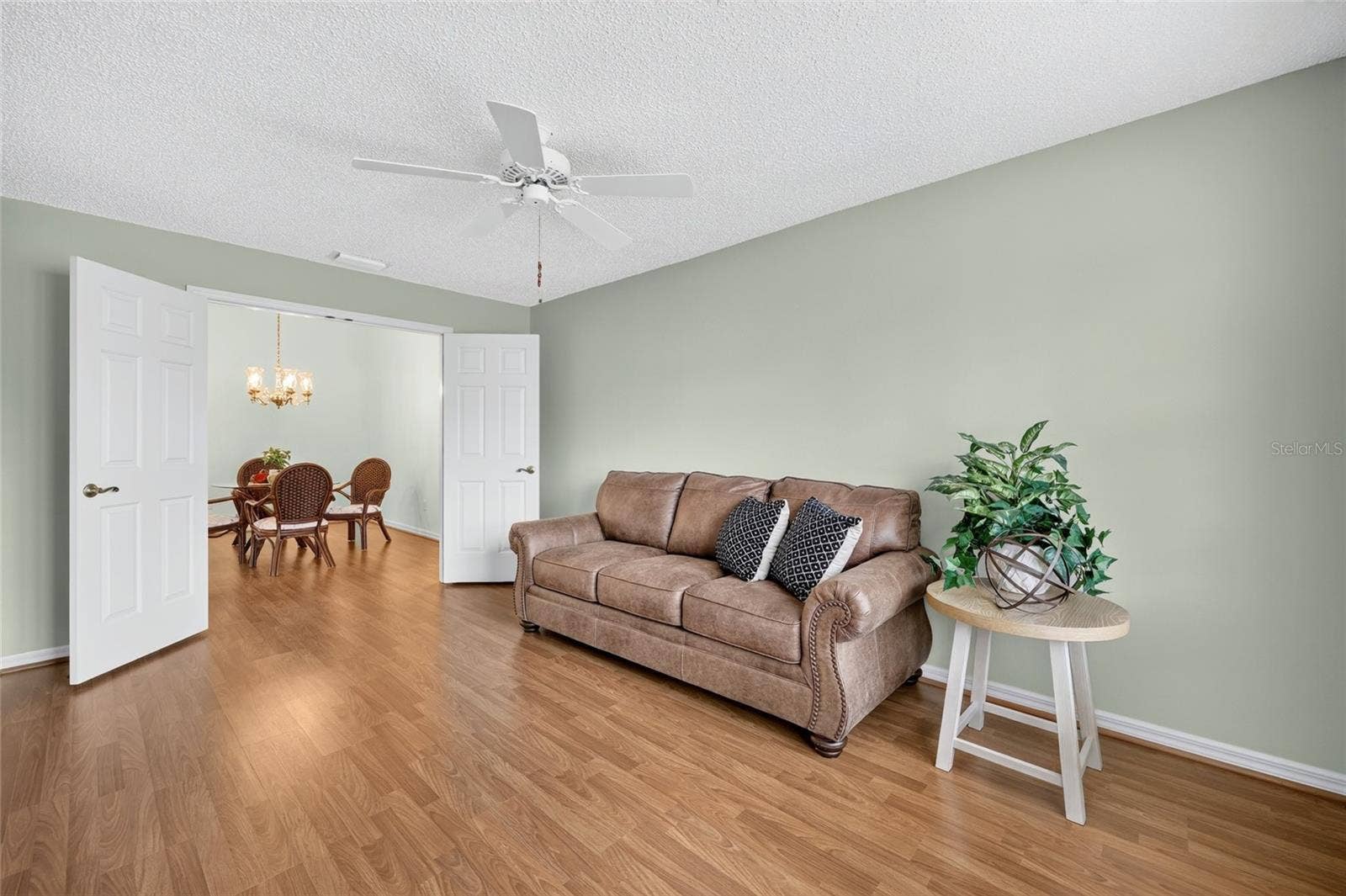 3064 BURBANK LANE, The Villages, FL 32162 Versatile room featuring wood-look flooring, a ceiling fan, soft neutral wall colors, and double doors opening to the dining area. Ideal for a home office, den, bedroom, or additional living space.