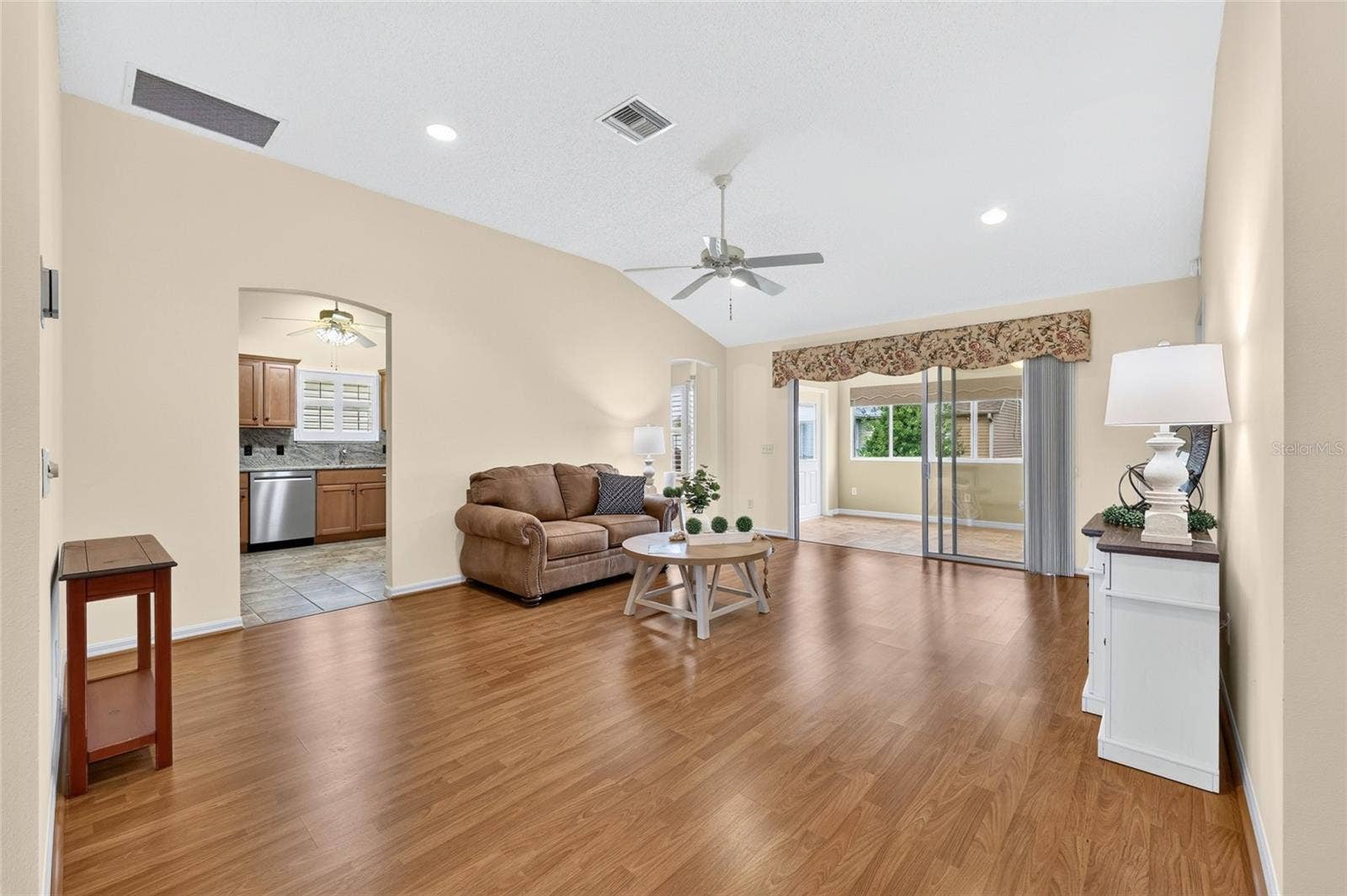 3064 BURBANK LANE, The Villages, FL 32162 Bright, spacious living room featuring vaulted ceilings, wood-look flooring, recessed lighting, and sliding glass doors leading to the enclosed lanai.