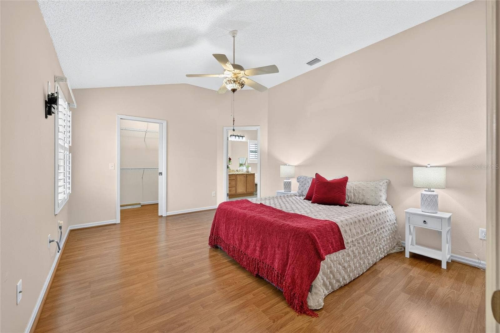 3064 BURBANK LANE, The Villages, FL 32162 Spacious primary suite featuring vaulted ceilings, wood-look flooring, a decorative ceiling fan, and convenient access to the walk-in closet and en-suite bathroom.