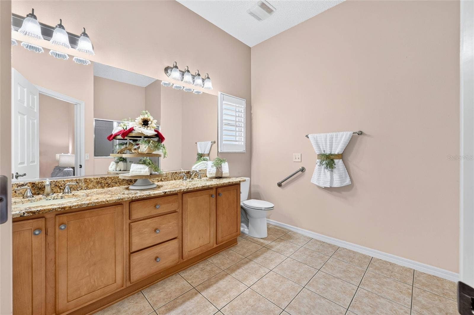 3064 BURBANK LANE, The Villages, FL 32162 Primary bathroom featuring a double-sink vanity with granite countertops, generous cabinet storage, tile flooring, and a large vanity mirror.