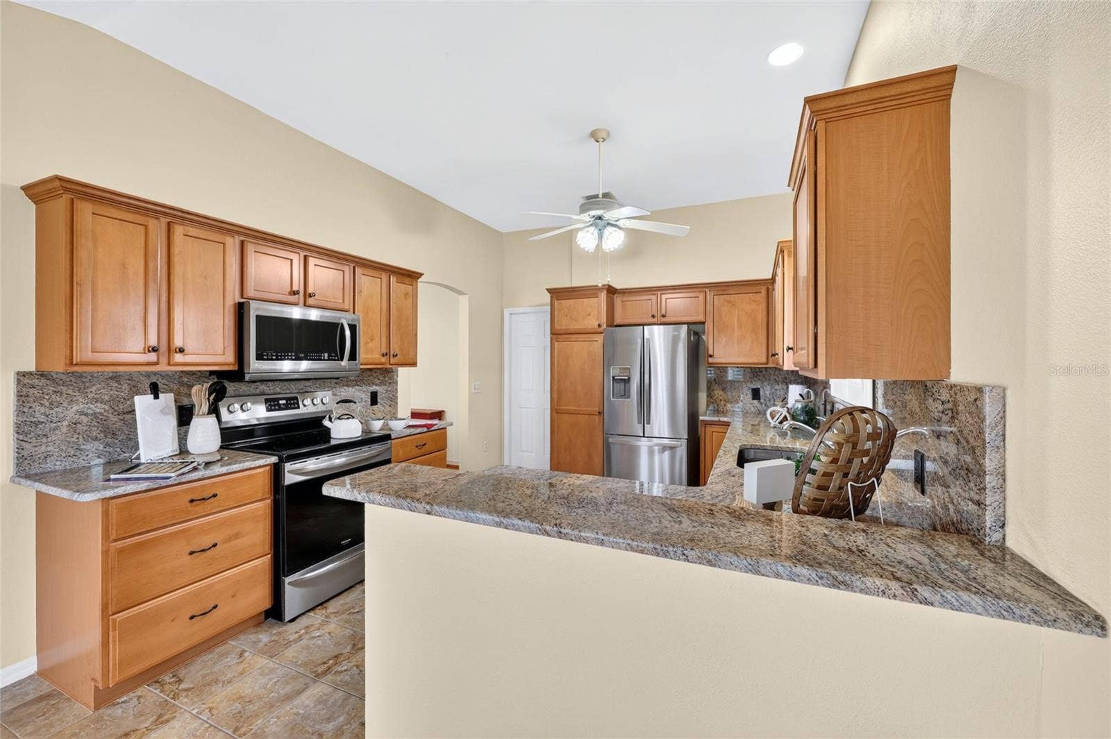 3064 BURBANK LANE, The Villages, FL 32162 Well-appointed kitchen featuring granite countertops and backsplash, warm wood cabinetry, stainless steel appliances, and a convenient breakfast bar.