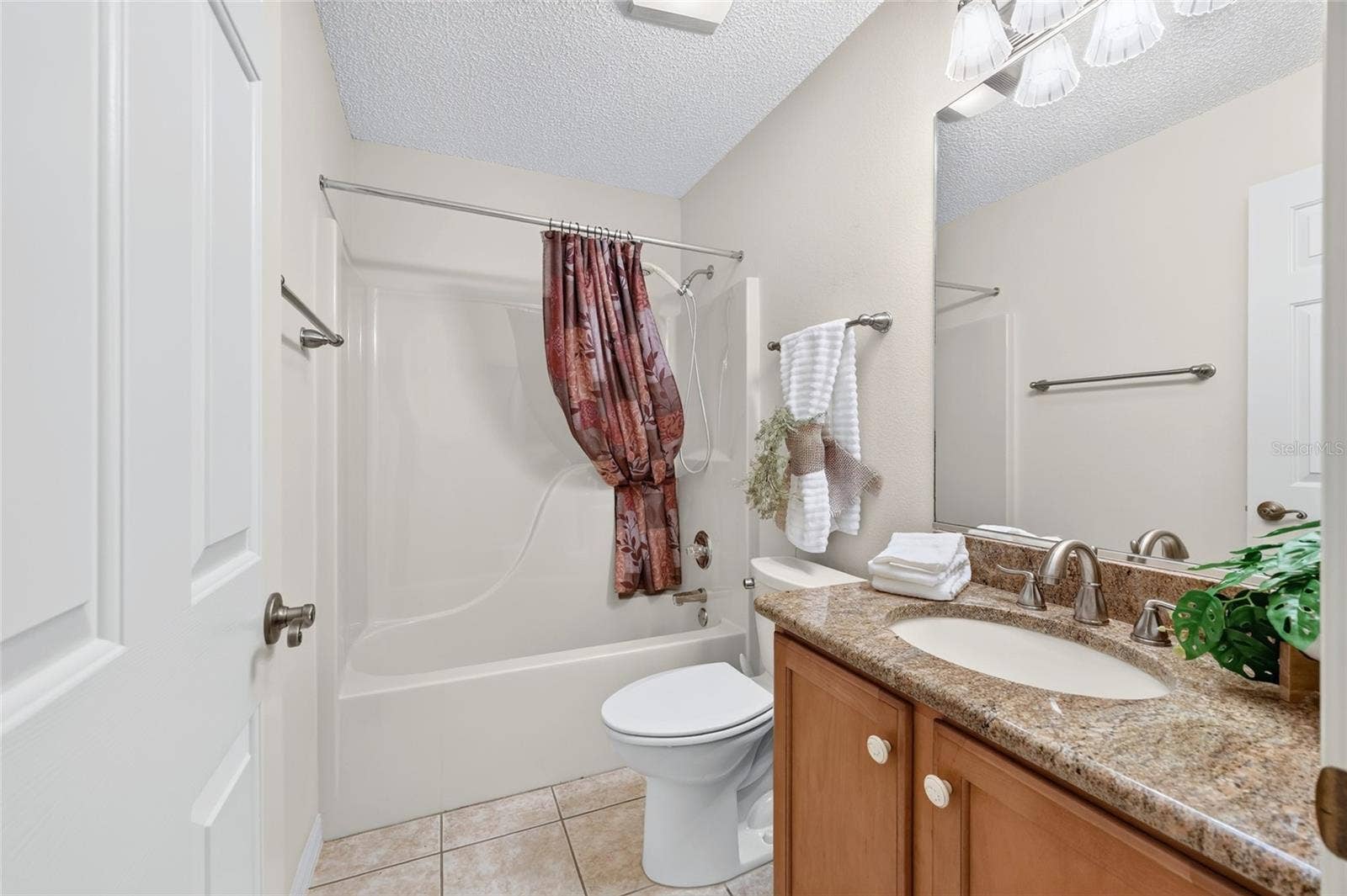 3064 BURBANK LANE, The Villages, FL 32162 Guest bathroom featuring a granite-topped vanity, wood cabinetry, tile flooring, and a combination bathtub and shower.