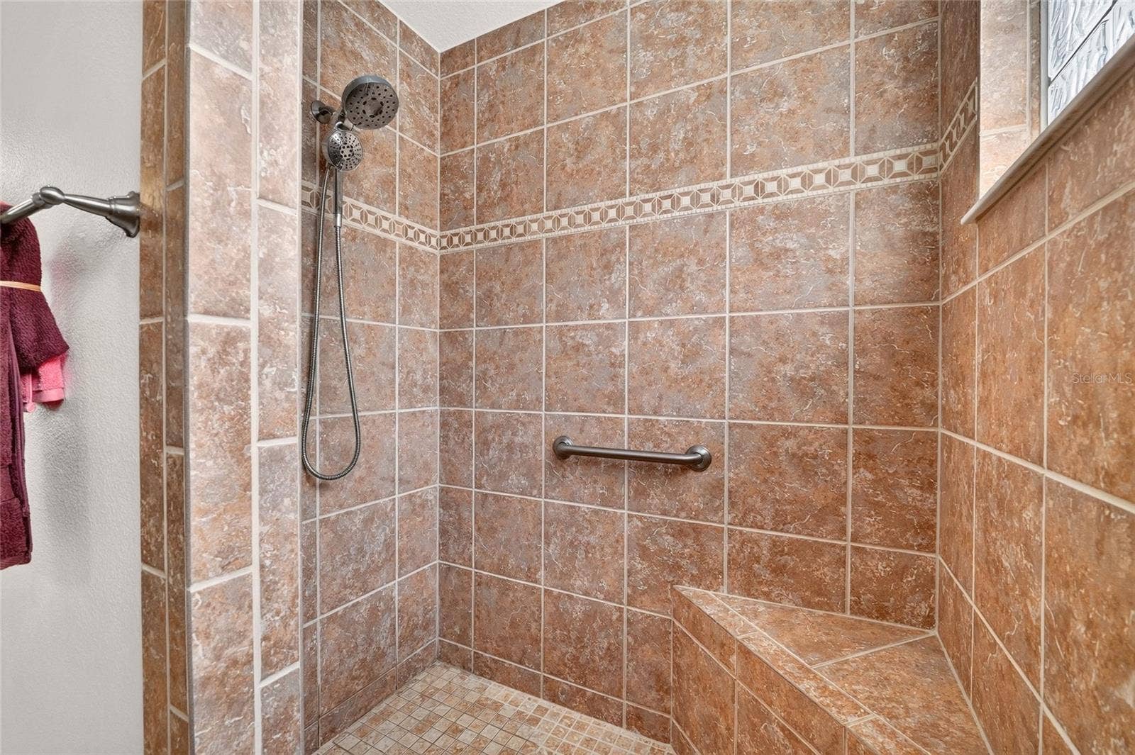 2454 MORNING DOVE LANE, The Villages, FL 32162 Enjoy a spacious ROMAN SHOWER with a convenient bench, decorative tile accents, and a GLASS-BLOCK WINDOW that welcomes natural light while maintaining privacy.
