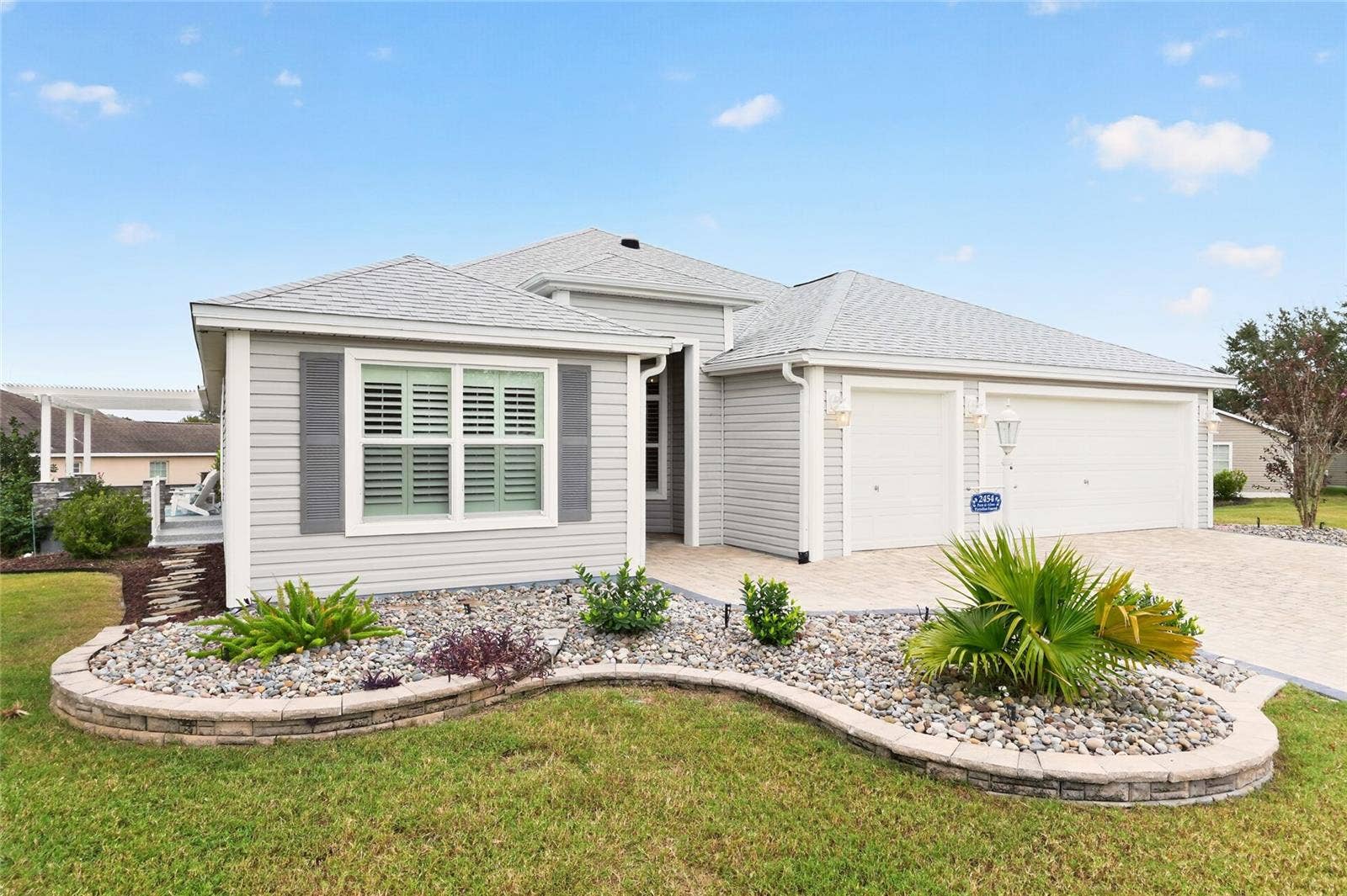 2454 MORNING DOVE LANE, The Villages, FL 32162 Beautifully tiered landscaping with decorative stone and tropical plantings complements the paver driveway and two-car plus golf cart garage, creating a welcoming first impression.