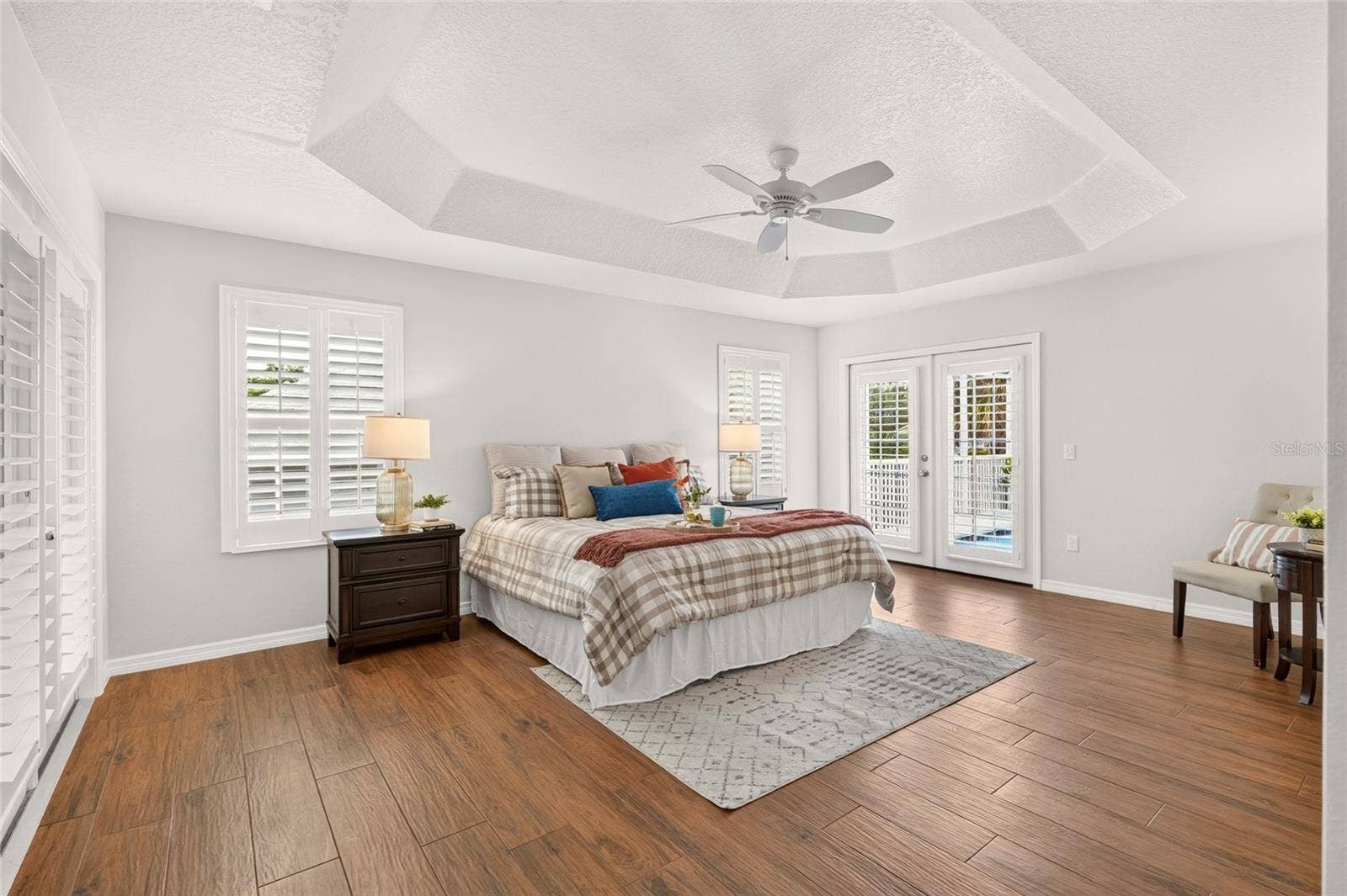2454 MORNING DOVE LANE, The Villages, FL 32162 The spacious PRIMARY SUITE features an elegant TRAY CEILING, PLANTATION SHUTTERS, and French doors leading to the pool for a refreshing start or relaxing end to your day.