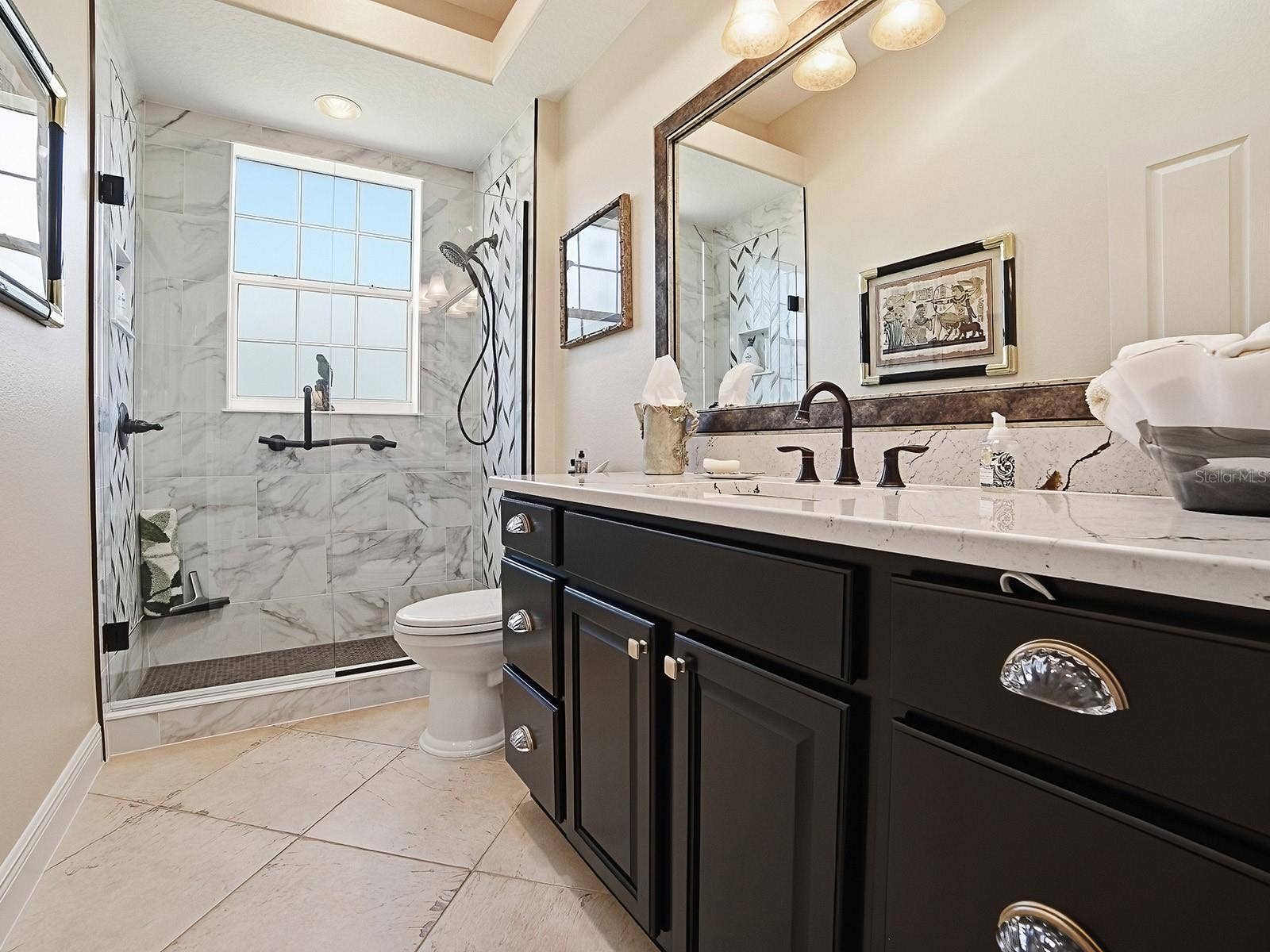 1103 MIONA SHORES DRIVE, The Villages, FL 32162 LOVELY RENOVATED GUEST BATH WITH FRAMELESS GLASS DOOR TO THE TILED SHOWER, QUARTZ COUNTERS FRAMED MIRROR AND NEW LIGHT FIXTURE. ALL OF THE TOILETS IN THE HOME ARE ALL A NEW TALLER STYLE.