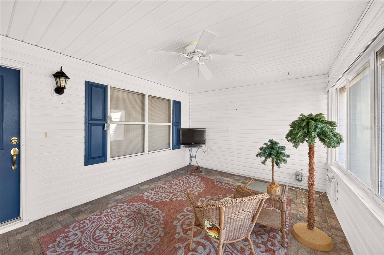 Charming enclosed front porch featuring brick-paver flooring, a ceiling fan, abundant windows, and comfortable seating space. An inviting area to relax and enjoy the Florida lifestyle.