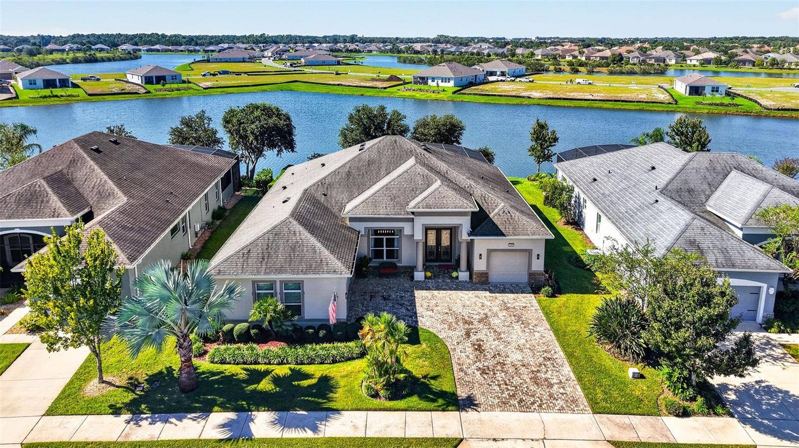 2444 PAWTUCKET PASS, Mount Dora, FL 32757 An aerial drone view highlights the front exterior of the home, framed by a serene lake backdrop.