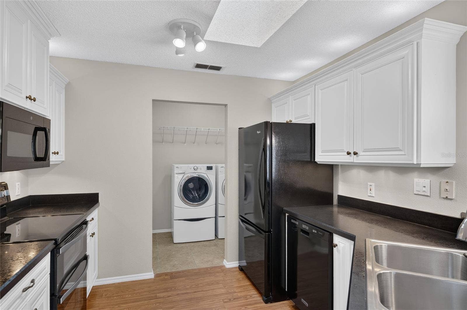 KITCHEN View - Showcases raised-panel white cabinetry with crown molding and over & under cab lights. A SKYLIGHT illuminates the kitchen w/ NATURAL LIGHT. Note that black appliances provide a dramatic contrast of color.