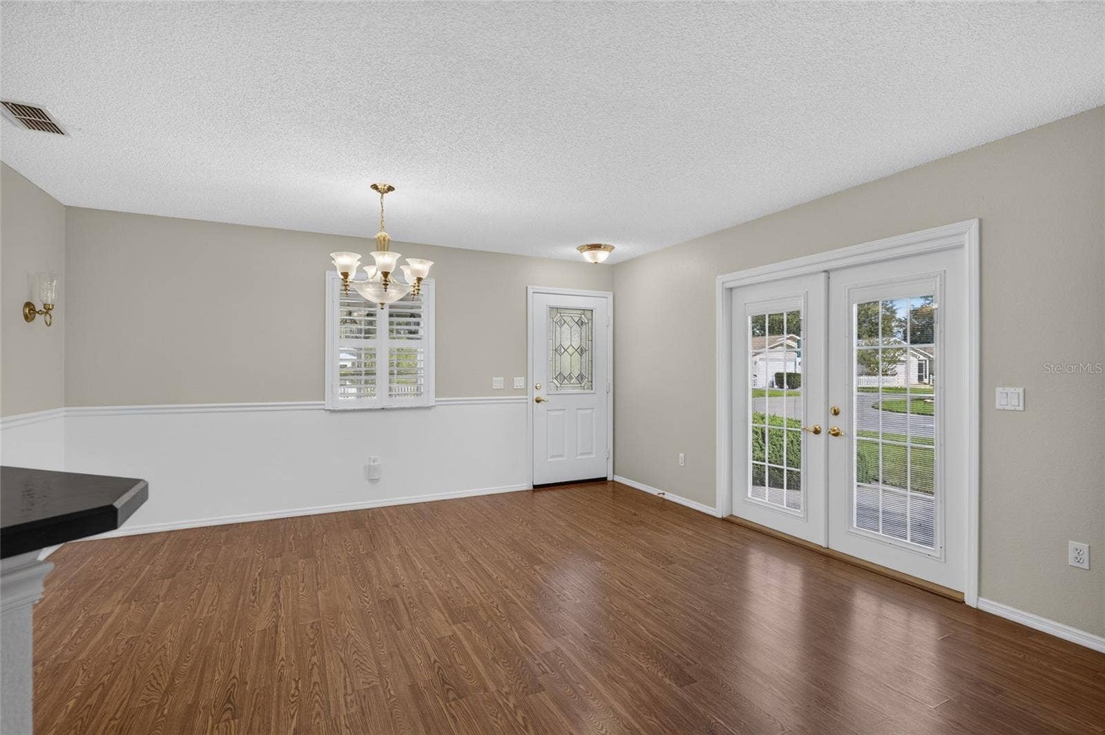 Close up view of DINING ROOM - Chair rail woodwork, decorative wall sconces (back L), and matching chandelier & pendant lighting add distinctive detail. Note the French doors which access the side patio on eastern side of home.