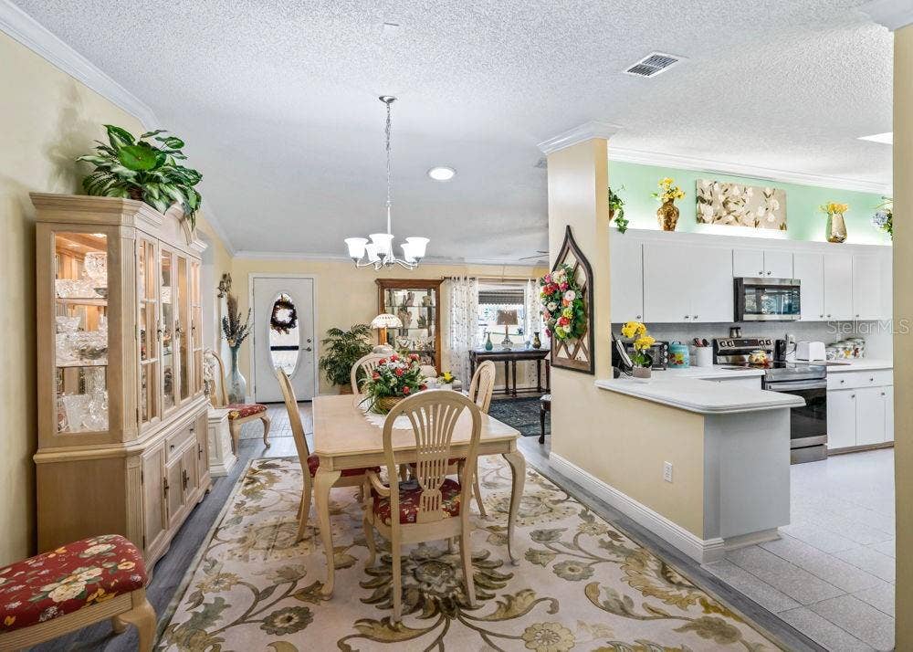 17909 SE 99TH AVENUE, Summerfield, FL 34491 Inviting dining space with wood-look flooring, crown molding, and chandelier lighting opens to the living room and kitchen.