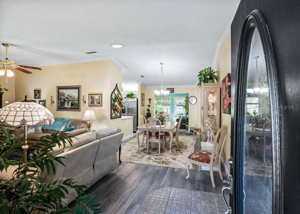 17909 SE 99TH AVENUE, Summerfield, FL 34491 Welcoming entry opens to a bright living and dining area featuring wood-look vinyl flooring, crown molding, and soft neutral tones. The open layout offers an inviting flow, with views toward the kitchen and sunlit rear living space.