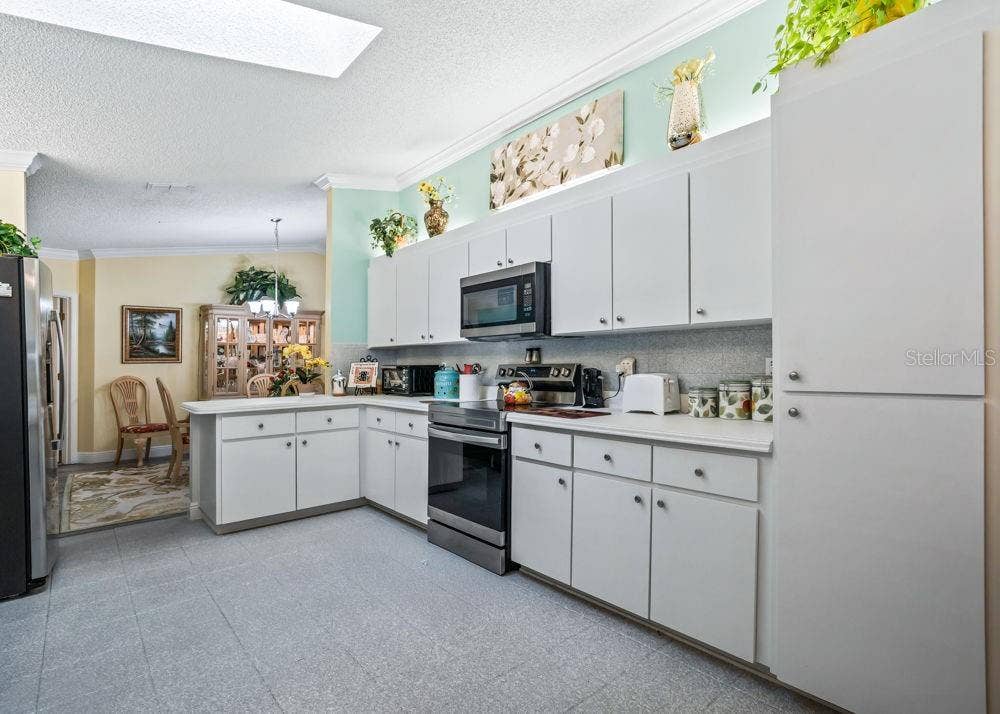17909 SE 99TH AVENUE, Summerfield, FL 34491 Inviting kitchen with white cabinetry, generous counter space, a tall pantry cabinet, and stainless steel appliances. A skylight brightens the space, while aqua accents and crown molding add charm. The adjoining dining area offers a convenient flow for meals and entertaining.