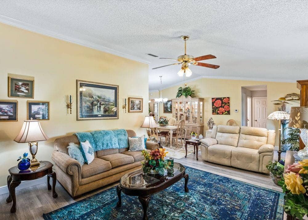 17909 SE 99TH AVENUE, Summerfield, FL 34491 Inviting living area featuring wood-look vinyl flooring, crown molding, soft neutral walls, and a ceiling fan. The open layout connects seamlessly to the dining area, creating a comfortable space for everyday living and entertaining.
