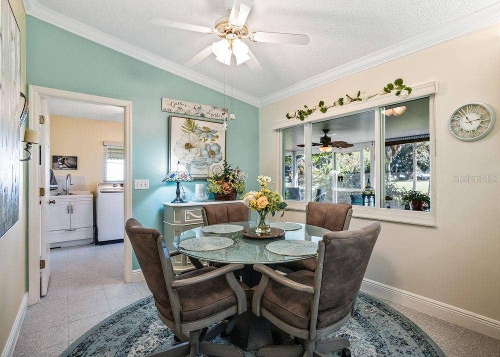 17909 SE 99TH AVENUE, Summerfield, FL 34491 Charming breakfast nook featuring a soft aqua accent wall, crown molding, and a ceiling fan. A large interior window overlooks the enclosed lanai and greenery beyond, while the adjacent laundry room adds everyday convenience.