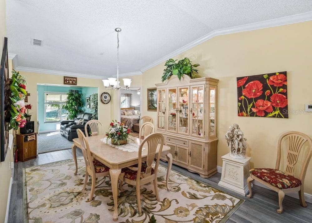 17909 SE 99TH AVENUE, Summerfield, FL 34491 Inviting dining area featuring wood-look vinyl flooring, crown molding, and a vaulted ceiling with a chandelier. The open layout flows into a sunlit sitting area, creating a welcoming space for everyday meals and entertaining.