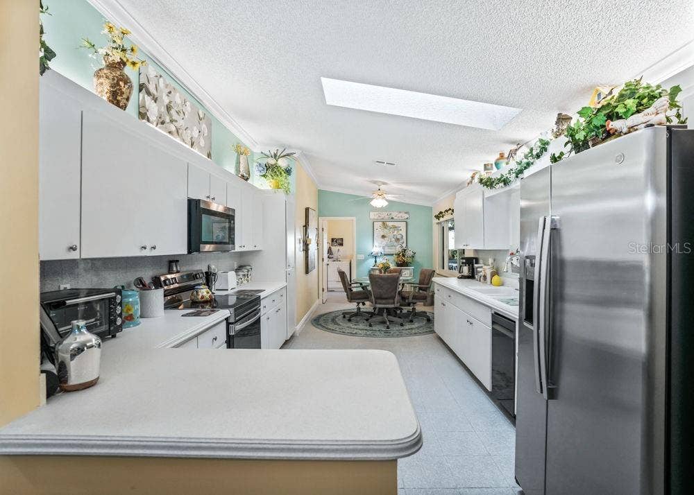 17909 SE 99TH AVENUE, Summerfield, FL 34491 Bright kitchen featuring white cabinetry, stainless steel appliances, ample counter space, and a convenient breakfast bar. A skylight brings in natural light, while the adjoining breakfast nook offers a comfortable spot for casual dining.