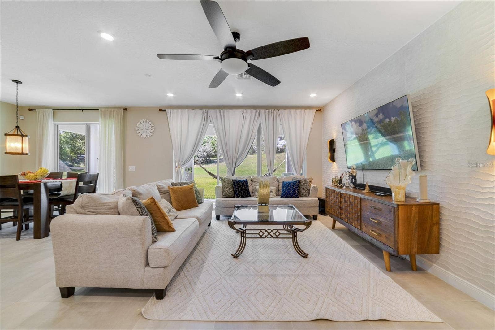 In the living room, enjoy a CUSTOM ACCENT WALL (2023) and views of the large backyard through dual sliding glass doors.