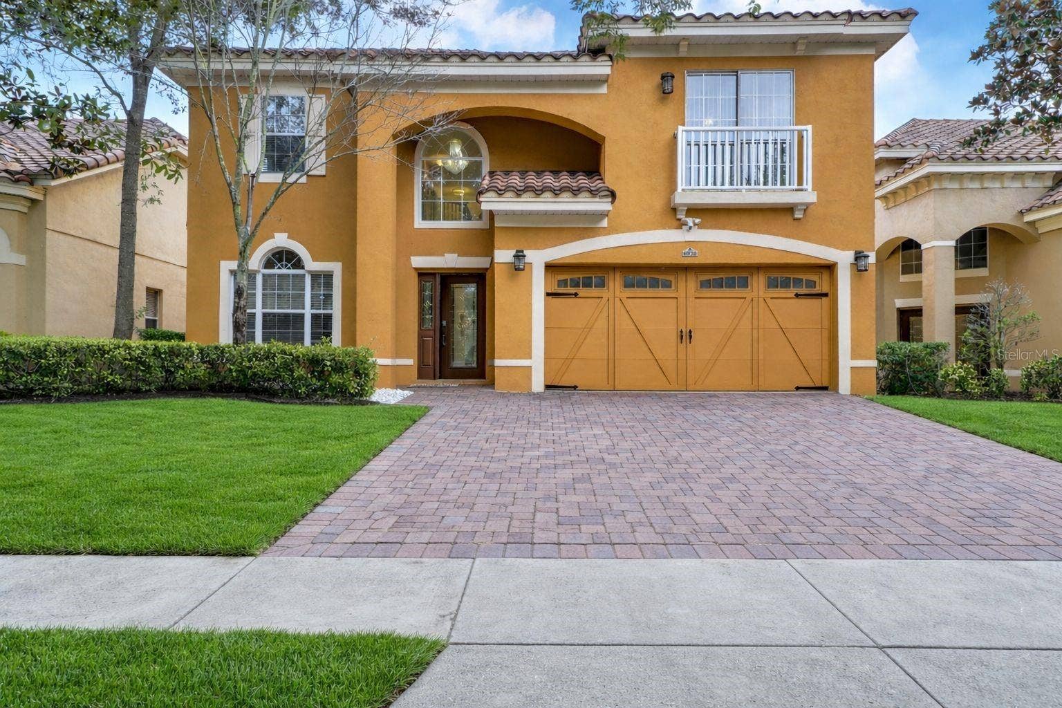 6956 LUCCA STREET, Orlando, FL 32819 A brick paver driveway leading to a spacious two-car garage with decorative carriage-style doors and black hardware accents.