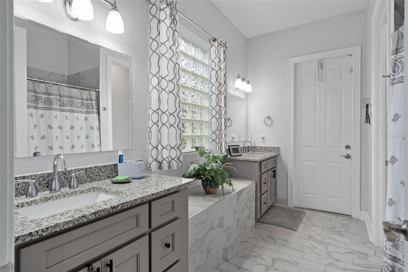 9057 BALMORAL MEWS SQUARE, Windermere, FL 34786 Downstairs Primary Bath fully upgraded with all new his/hers vanities and custom floor tile. Also has a door leading to the rear of the home.