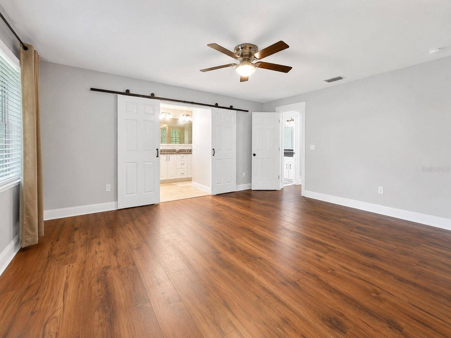 14140 COUNTRY ESTATE DRIVE, Winter Garden, FL 34787 Spacious primary suite with warm wood-like flooring, soft natural light, and charming barn doors leading into the private bathroom retreat.