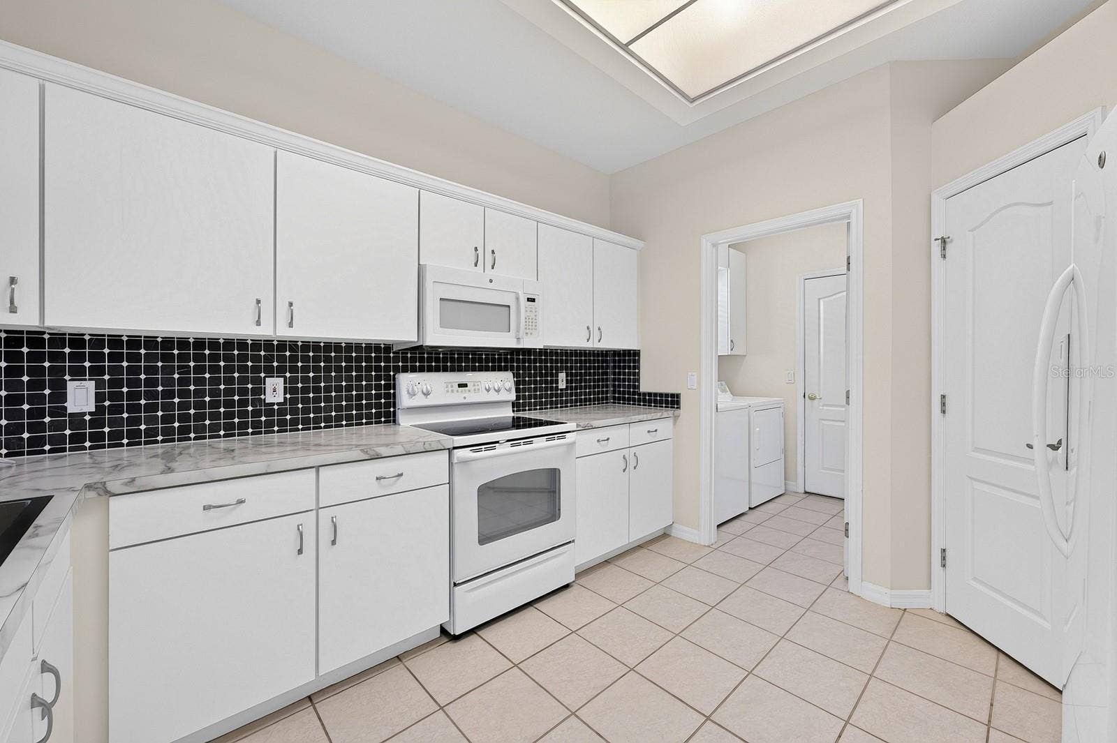 The spacious Kitchen, REFRESHED IN 2024, offers plenty to appreciate, including newer countertops, updated cabinet hardware and crown molding, a newer large sink and a tile backsplash.