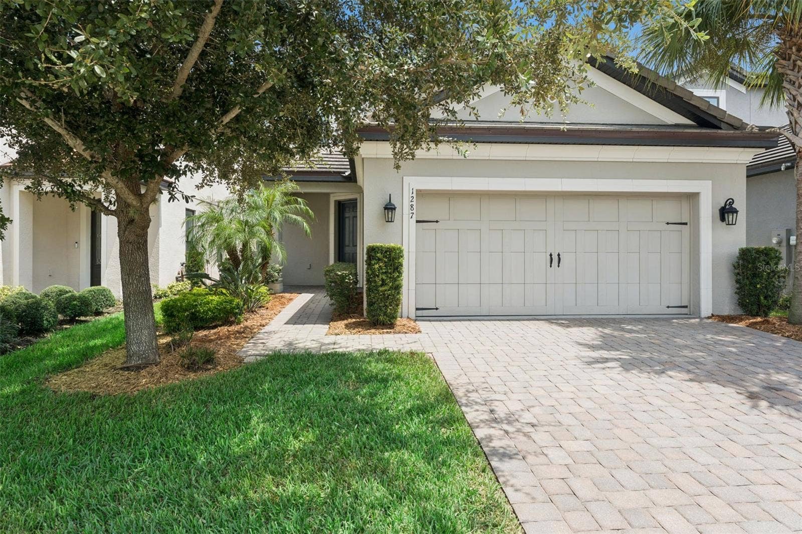 Front Exterior  Welcoming front exterior with mature landscaping, a paver driveway, and a two-car garage with carriage-style detailing.