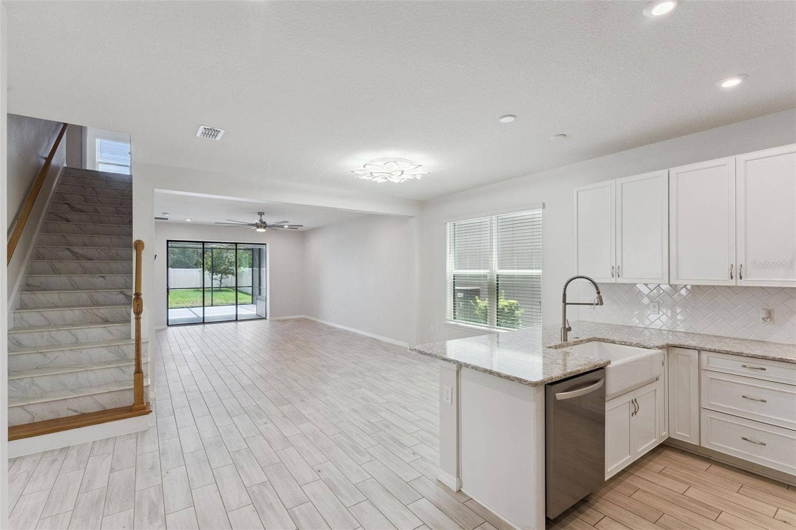 Kitchen & Main Living Area  Wide view highlights the home's open layout, with the kitchen flowing into the spacious living area and sliding glass doors extending the sightline to the screened patio and backyard.