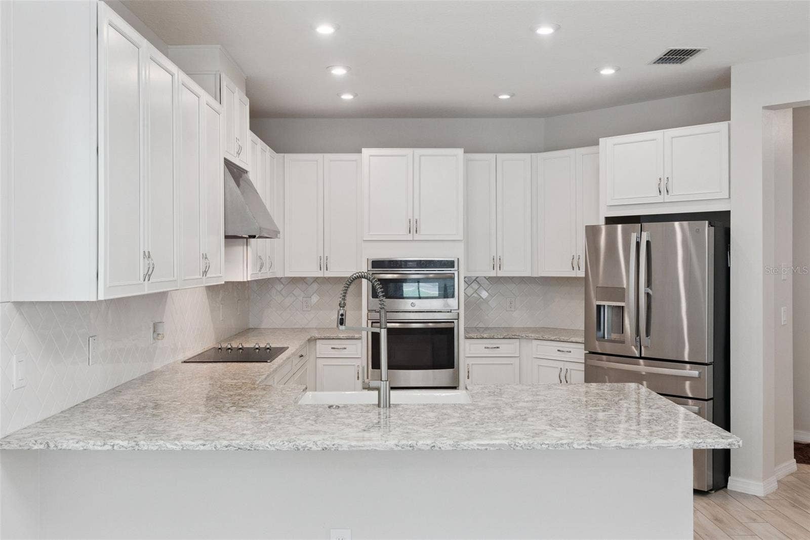 Kitchen  Spacious kitchen features abundant white cabinetry, granite countertops, a classic tile backsplash, stainless steel appliances, double wall ovens, and a generous peninsula with farmhouse-style sink and statement faucet.