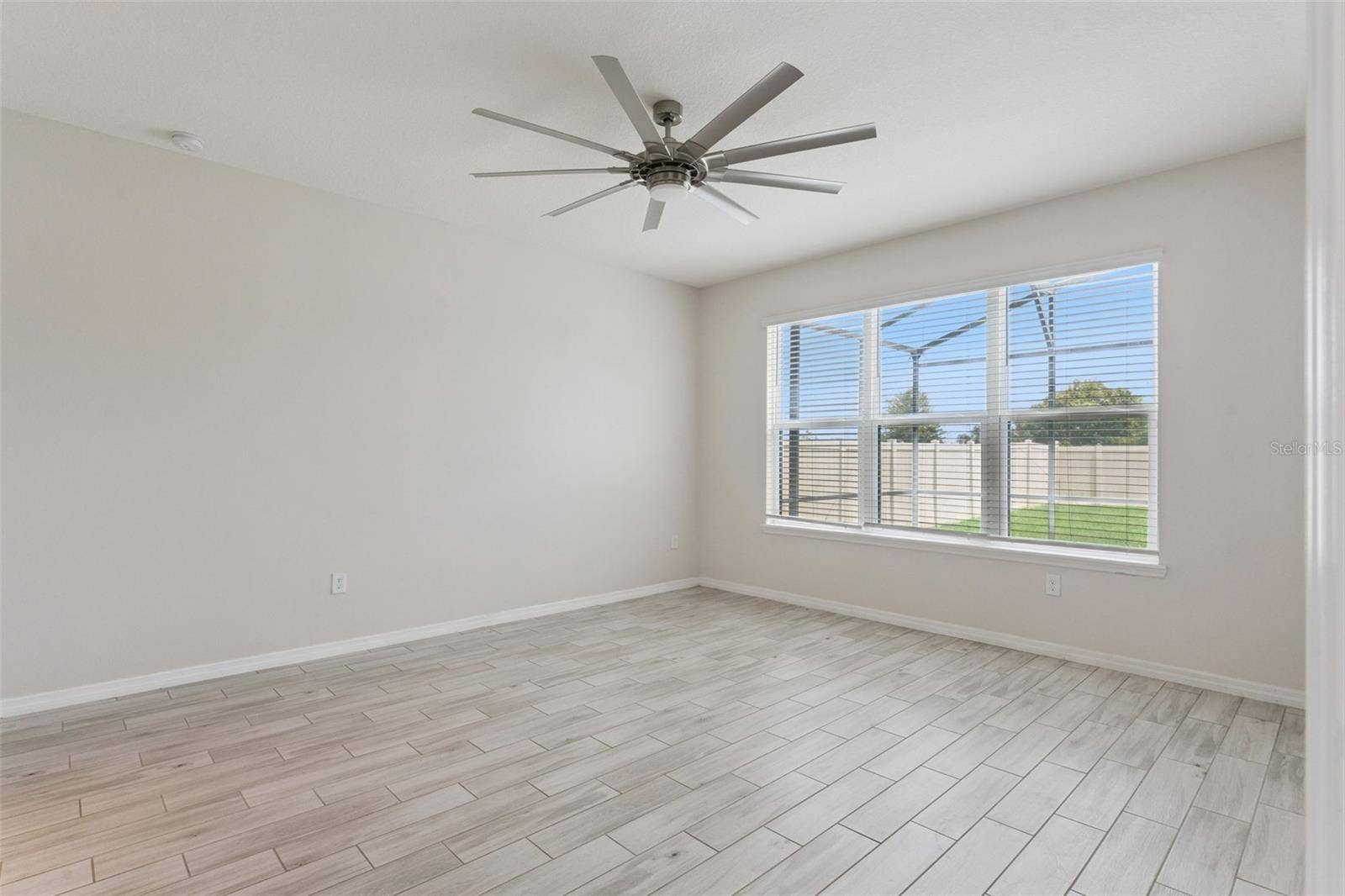 Primary Bedroom  Main-level primary bedroom offers generous proportions, wood-look tile flooring, a statement ceiling fan, and a wide window bringing in abundant natural light.