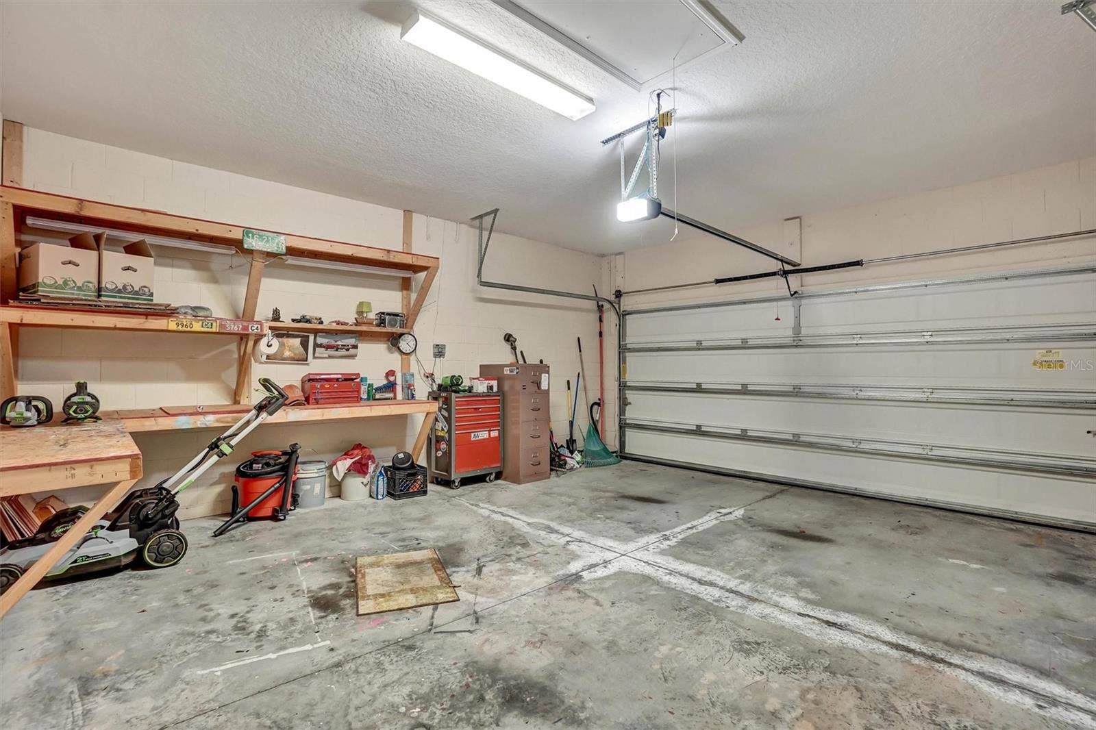 Large garage with overhead storage, workbenches, and an automatic garage door.