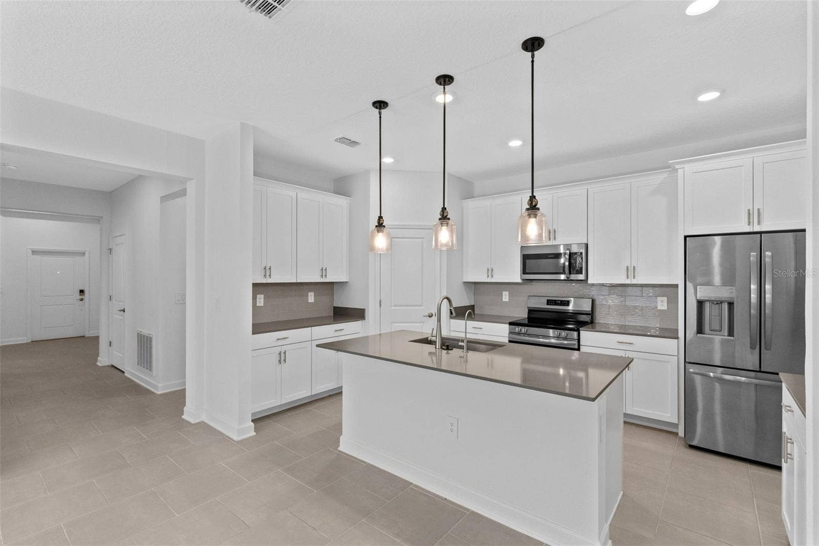 1874 FLOURISH AVENUE, Kissimmee, FL 34744 At the heart of the home, the kitchen features shaker style cabinetry, quartz countertops, stainless steel appliances, a tiled backsplash, pantry storage and a large island with breakfast bar seating beneath pendant lighting.