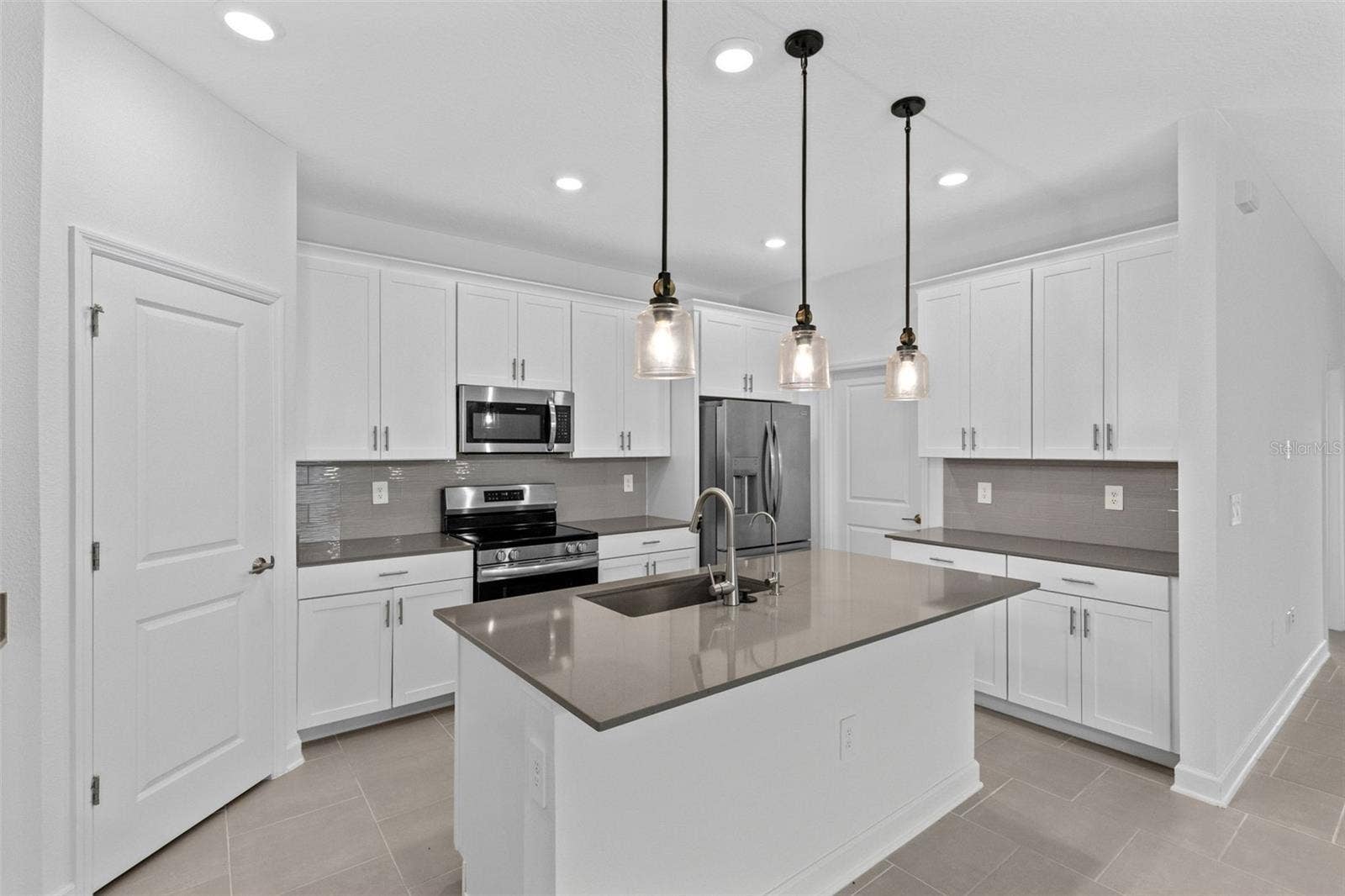 1874 FLOURISH AVENUE, Kissimmee, FL 34744 At the heart of the home, the kitchen features shaker style cabinetry, quartz countertops, stainless steel appliances, a tiled backsplash, pantry storage and a large island with breakfast bar seating beneath pendant lighting.