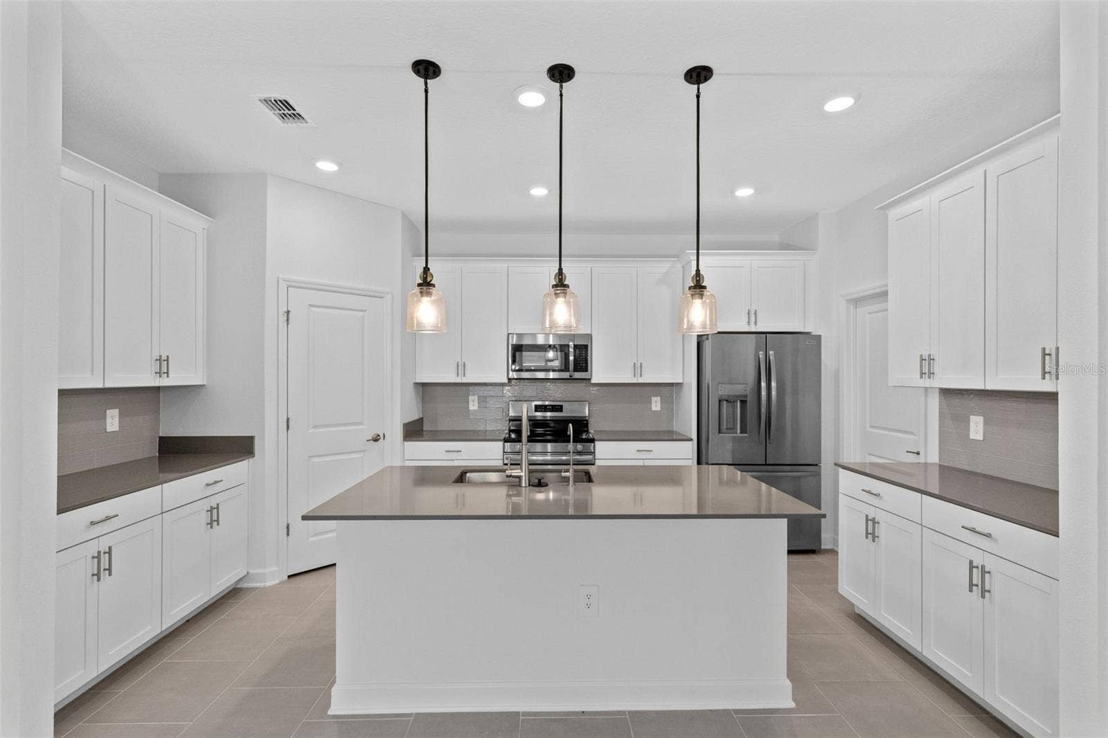 1874 FLOURISH AVENUE, Kissimmee, FL 34744 At the heart of the home, the kitchen features shaker style cabinetry, quartz countertops, stainless steel appliances, a tiled backsplash, pantry storage and a large island with breakfast bar seating beneath pendant lighting.