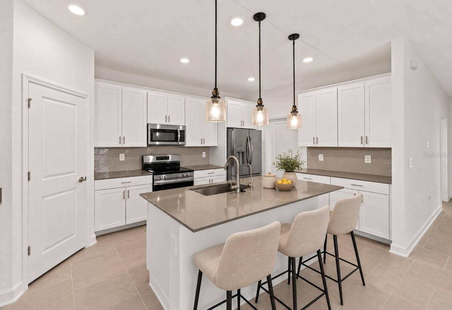 1874 FLOURISH AVENUE, Kissimmee, FL 34744 At the heart of the home, the kitchen features shaker style cabinetry, quartz countertops, stainless steel appliances, a tiled backsplash, pantry storage and a large island with breakfast bar seating beneath pendant lighting.