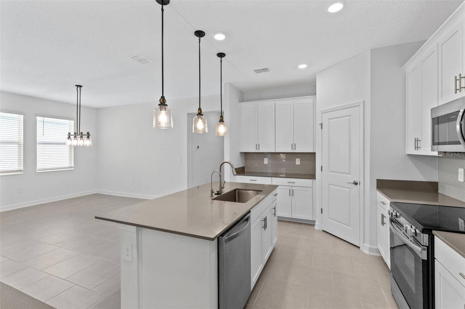 1874 FLOURISH AVENUE, Kissimmee, FL 34744 At the heart of the home, the kitchen features shaker style cabinetry, quartz countertops, stainless steel appliances, a tiled backsplash, pantry storage and a large island with breakfast bar seating beneath pendant lighting.