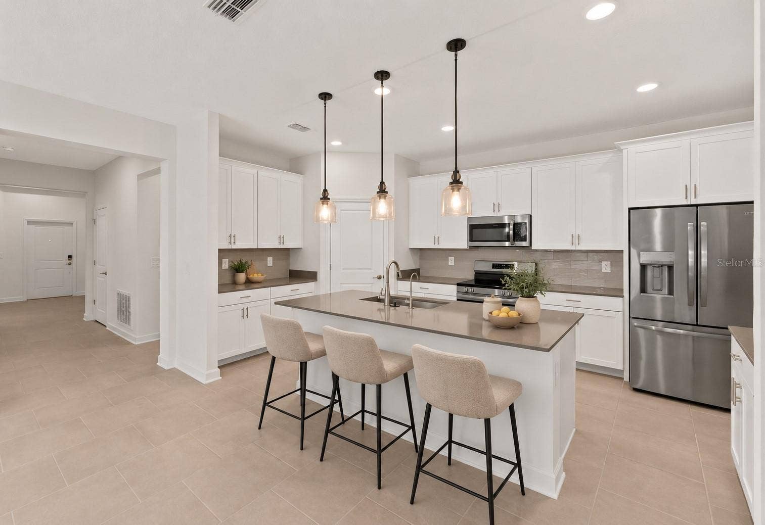1874 FLOURISH AVENUE, Kissimmee, FL 34744 At the heart of the home, the kitchen features shaker style cabinetry, quartz countertops, stainless steel appliances, a tiled backsplash, pantry storage and a large island with breakfast bar seating beneath pendant lighting.