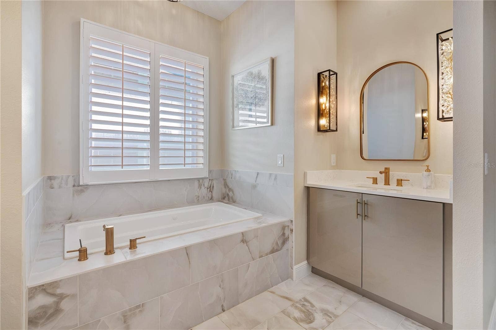 17600 LAKE STAR ROAD, Winter Garden, FL 34787 Relaxing bath retreat with a soaking tub beneath plantation shutters, decorative mirror and gold-tone fixtures.