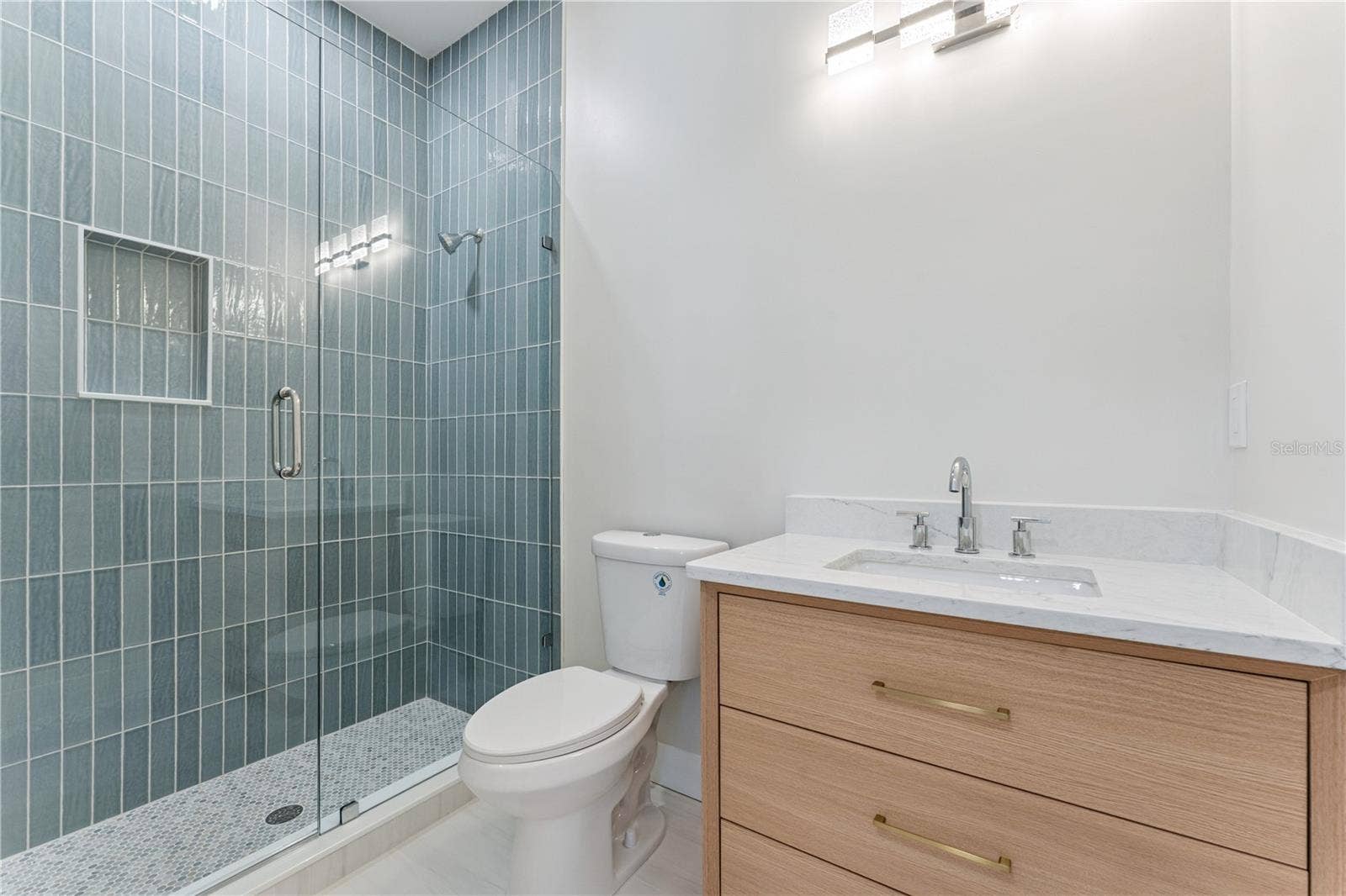 3456 FAIRWAY LANE, Orlando, FL 32804 Blue shower tile and a wood-toned vanity add color and warmth to this bathroom.