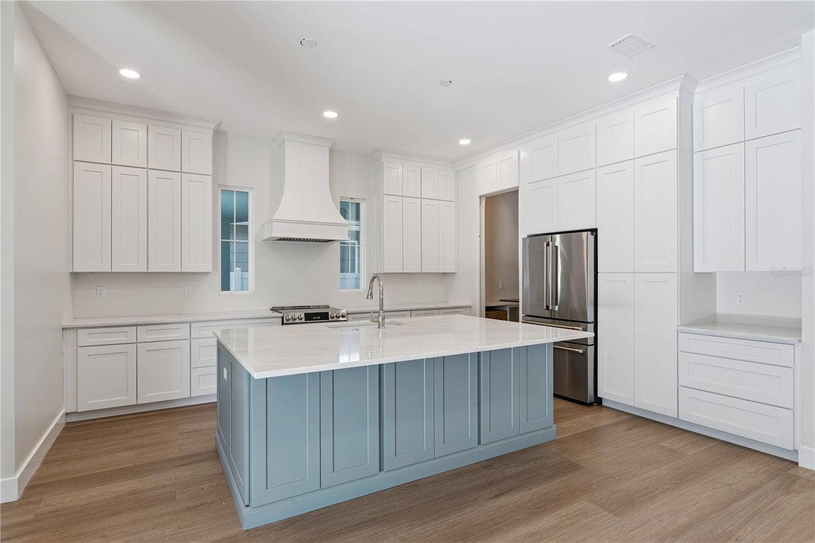 3456 FAIRWAY LANE, Orlando, FL 32804 The main kitchen features a blue island, white cabinetry, a statement range hood, and stainless steel appliances.
